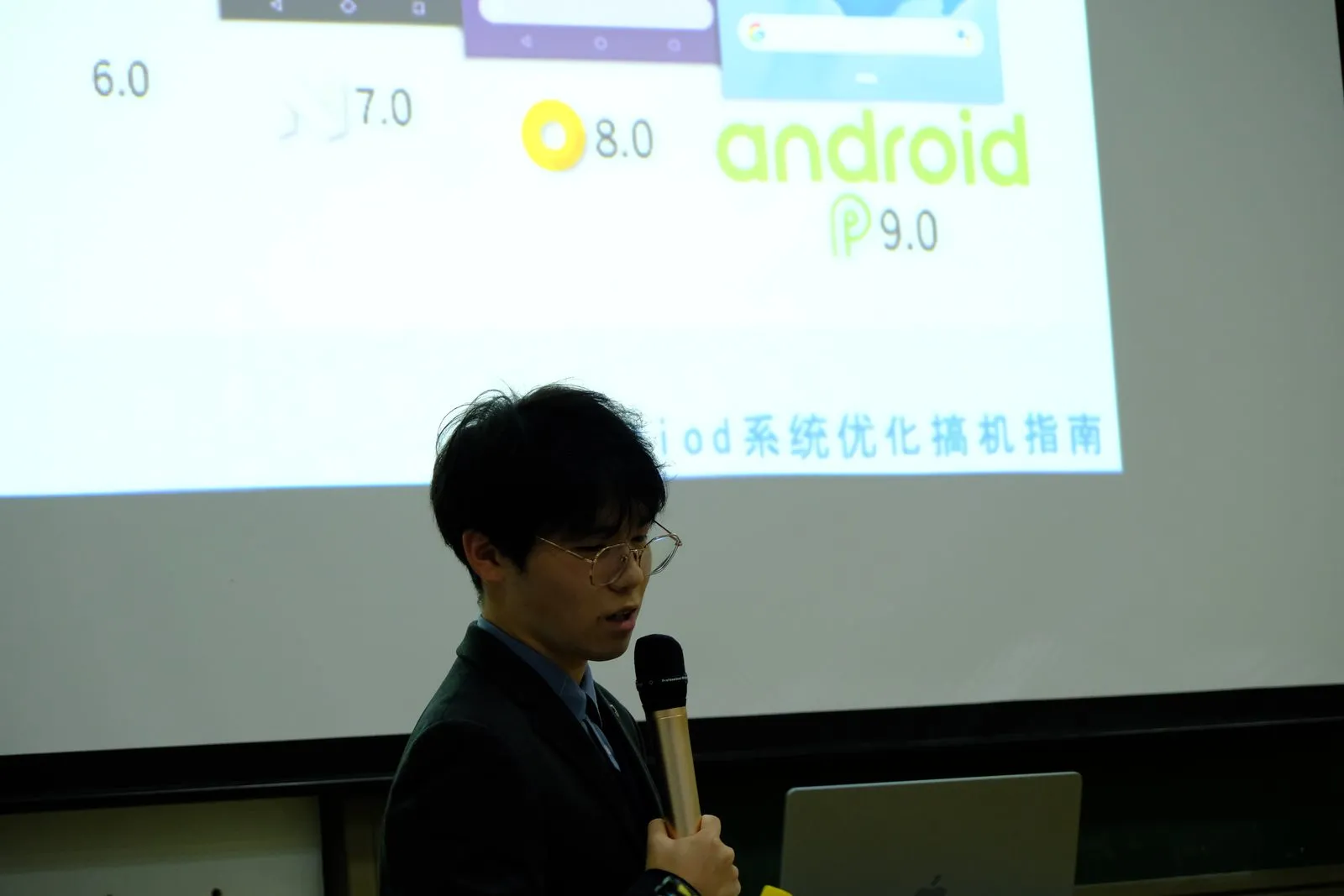 投影上并排展示 Android 6.0、7.0、8.0 与 Android P 9.0 的图标与界面,下方标题为系统优化搞机指南,讲者在画面前侧身讲解