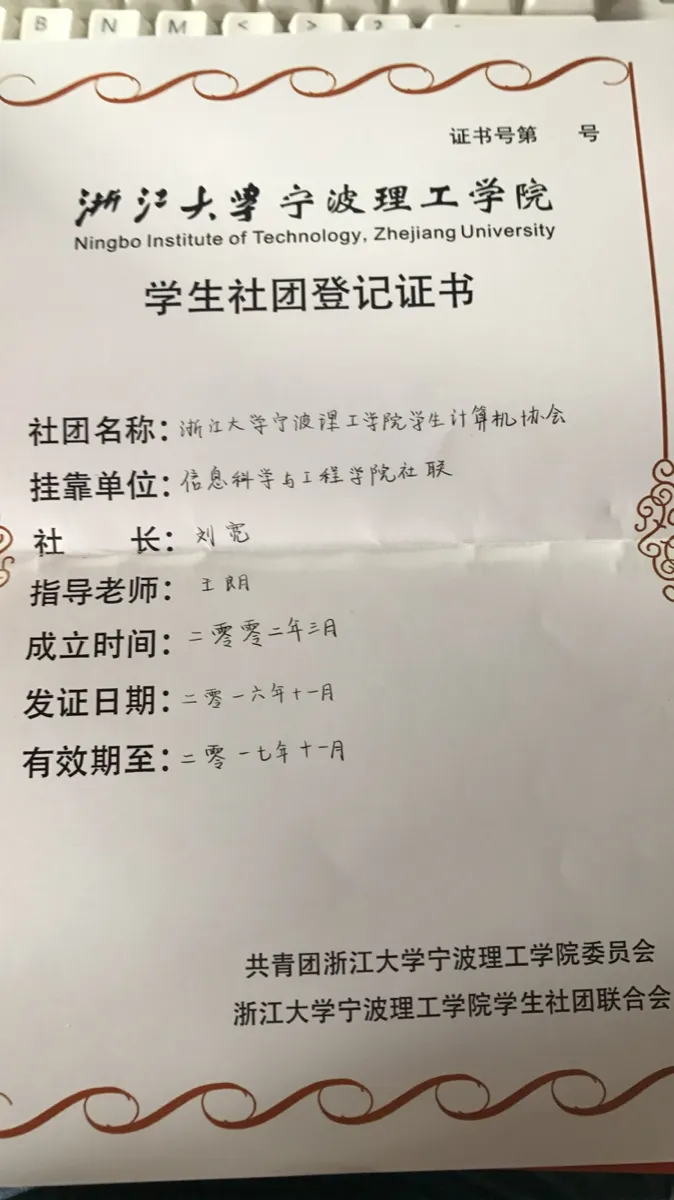 一张带橙色花边的证书照片，摆在键盘上拍摄；抬头是浙江大学宁波理工学院校徽与校名，标题“学生社团登记证书”，右上角“证书号第　号”一栏空着；正文各栏为手写填写