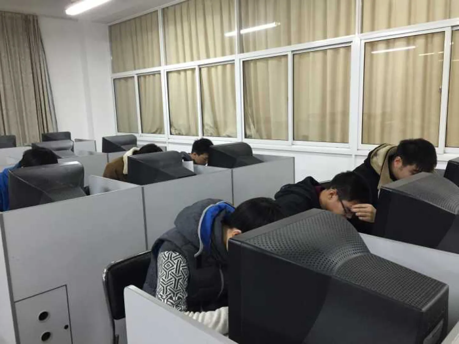 机房里一排排带隔板的机位,参赛学生分坐其间对着显示器答题,多数人穿着冬季外套,靠窗一侧拉着米色窗帘