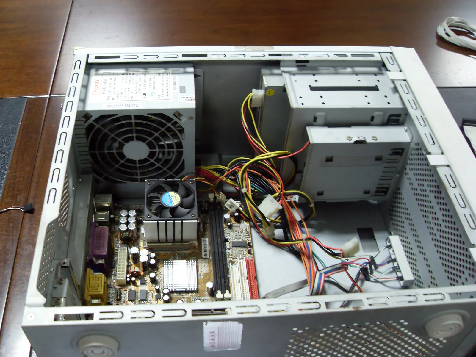 俯拍一台开盖的台式机内部：上方是 ATX 电源与散热风扇，中间主板上装着 CPU 散热器与内存插槽，右侧是光驱与硬盘支架，橙黄红黑的供电线与彩色前面板跳线散在机箱内