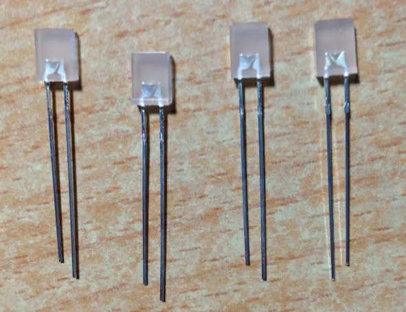 木纹桌面上并排四颗方形白色磨砂封装的 LED,引脚未剪,可见每颗都是一长一短两脚