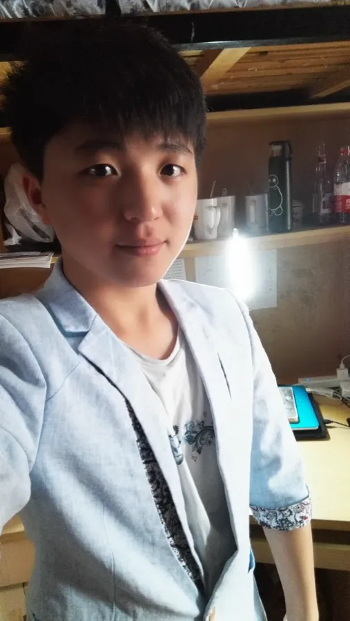 室内自拍:一名穿浅色外套的男生站在书桌前看向镜头