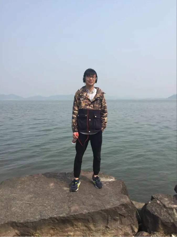 湖边的全身照:一名穿花衬衫的人站在一块伸入水面的岩石上,背景是开阔水面与远岸