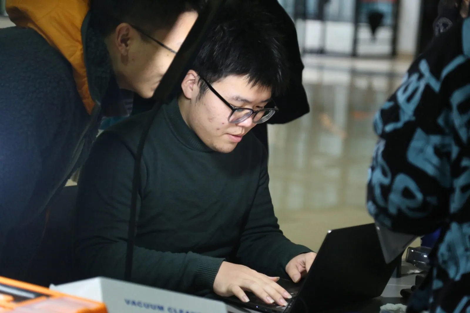 一名队员俯身在笔记本上操作,另一名队员在旁看着屏幕,桌上放着吸尘器包装盒