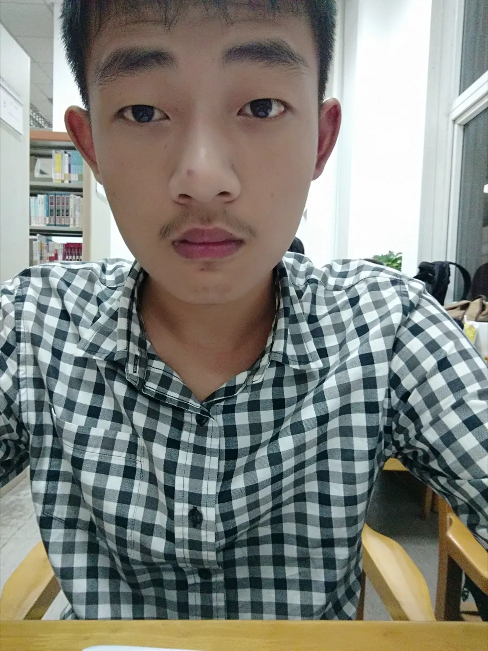 室内窗边的半身照,一名穿格子衬衫的男生正面对镜头